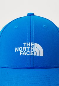Svetlomodrá baseballová čiapka s bielou vyšitou logom "The North Face" umiestneným na prednom panely.