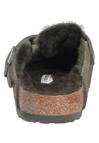 Calzado de ante verde con un interior suave forrado de pelo, suela de corcho y forma curva. Presenta un detalle de hebilla plateada en el lateral.