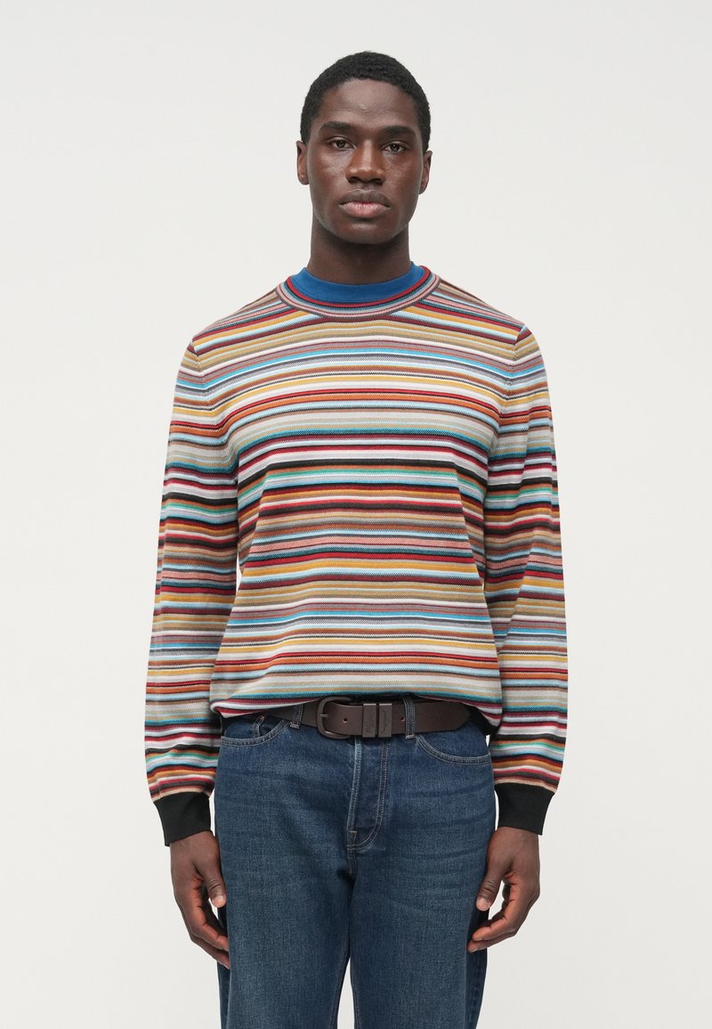 Maglione a righe con linee orizzontali multicolori. Il materiale sembra morbido. Presenta una scollatura rotonda e polsini neri. Abbinato a jeans blu.