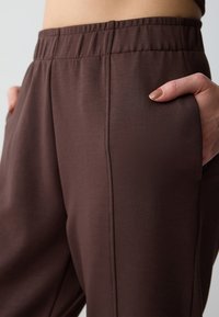 Lichte, bruine broek met een elastische tailleband. Beschikt over zijzakken en een gladde textuur, ideaal voor comfort en casual gebruik.