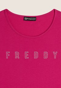 T-shirt fucsia con colletto rotondo e maniche corte, con la scritta "FREDDY" in lettere argentate sulla parte anteriore. Tessuto liscio e leggermente elasticizzato.