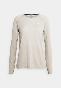 Ljust beige långärmad skjorta tillverkad av textil. Har en rund halsringning och en diskret logotyp på bröstet. Slätt, andningsbart material.