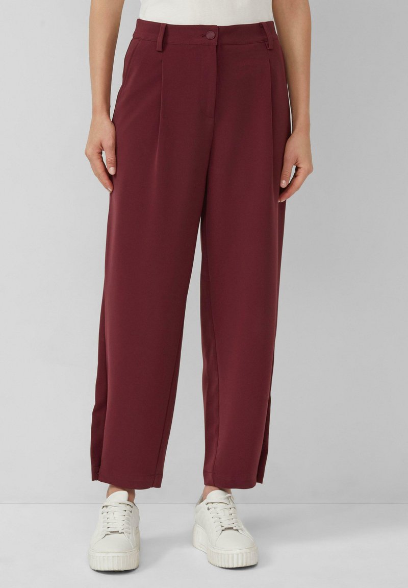 Pantalons larges bordeaux avec taille haute, dotés d'une fermeture à bouton et de poches latérales, associés à des sneakers blanches. Texture de tissu lisse.