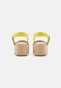 Sandalias de plataforma amarillas con suela de yute trenzado, que presentan un diseño de tiras sencillo y un acento de botón en la tira del talón.