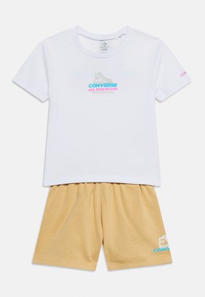 T-shirt blanc à manches courtes avec logo Converse All Star et short beige à taille élastique avec petit logo Converse sneaker sur la jambe.