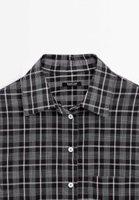 Czarna i biała koszula w kratę z klasycznym kołnierzykiem, zapinana na guziki, z kieszenią. Wykonana z gładkiego materiału o usystematyzowanym designie.