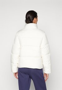 Witte pufferjack met een hoge kraag, voorzien van een boxy ontwerp, horizontale stiksels en een gladde textuur. Draagt bij navy broek.