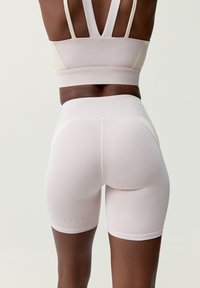 Ljusrosa träningsshorts med en figurvänlig design och sömlös textur; har hög midja och diskret sömnadsdetalj på sidorna.