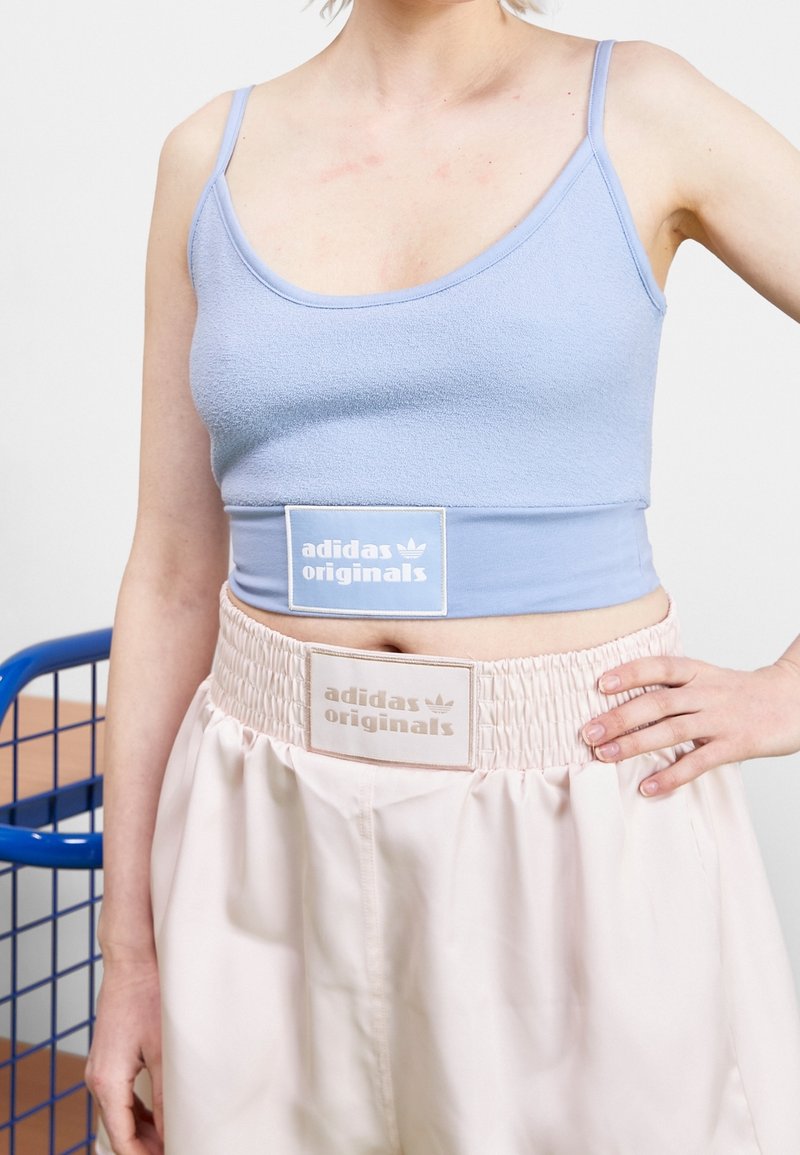 Světle modrý zkrácený top bez rukávů s texturovanou tkaninou, v kombinaci se světle růžovými šortkami s vysokým pasem, které mají elastický pas a nášivky s logem.