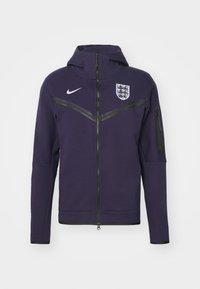 Veste à capuche zippée violette en tissu doux, avec une bande d'accent noire, le logo Nike et le blason de l'Angleterre sur la poitrine. Conception à capuche.