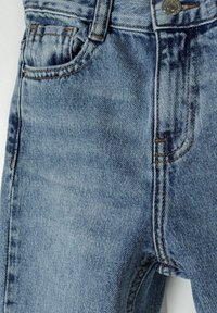 Gaiši zili džinsi ar klasisku piecu kabatu dizainu, redzamām šuvēm un metāla pogu aizdari, ar nelielu nolietojumu.