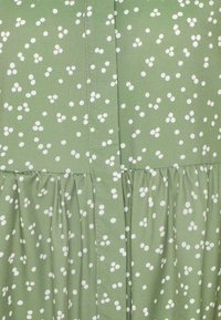Tissu vert avec un motif de points blancs en grappe et un détail de couture froncée traversant horizontalement le milieu.