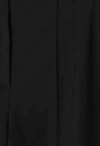 Zwarte stof met een gladde textuur en gestikte naaddetails. Het ontwerp heeft verticale lijnen en een slanke, op maat gemaakte vorm.