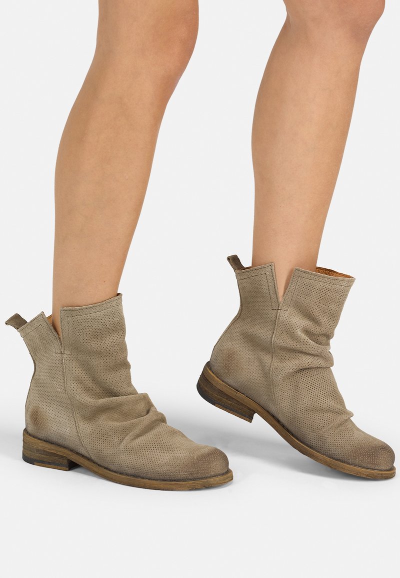 Botas de tobillo beige hechas de cuero perforado con un diseño arrugado, tacón bajo de madera y lengüetas para facilitar su uso.