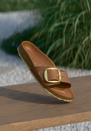 Brauner Rutschsandal aus Leder, mit einem breiten Riemen, einem goldenen Schnalle-Akzent und einer strukturierten Korksohle mit einer leichten Gummiunterseite.