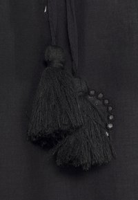 Two black fabric tassels hanging against a textured black cloth background with small circular cutout details nearby.