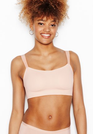 Giovane donna con capelli ricci che sorride, indossa un reggiseno senza cuciture color nude e slip coordinati su sfondo bianco.
