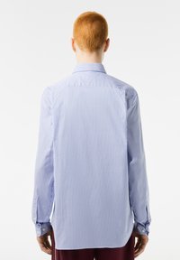 Camisa de manga larga a rayas azul claro y blanca con cuello abotonado y mangas con puños, hecha de una tela suave y con corte recto.