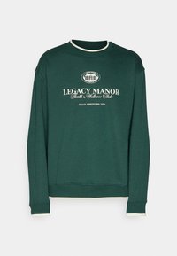 Grön sweatshirt i bomull med rundad halsringning. Har vita ribbade detaljer vid halsringningen och manschetterna. Tryckt logotypdetalj framtill.