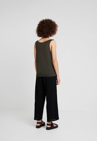 Canotte verde oliva in materiale morbido, abbinata a pantaloni neri larghi e texturizzati. Design semplice con spalline larghe e vestibilità comoda.