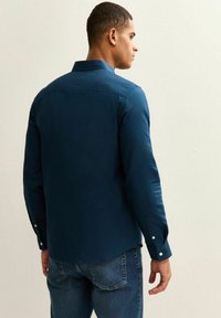 Navyblauw overhemd met lange mouwen, een gestructureerde kraag, knoopmanchetten en een gladde textuur, gecombineerd met lichtblauwe jeans.