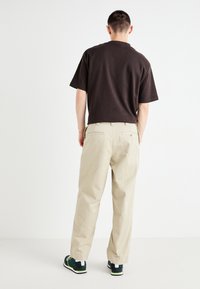 Black short-sleeve shirt paired with light beige trousers. The trousers have a relaxed fit and two back pockets, worn with dark sneakers.