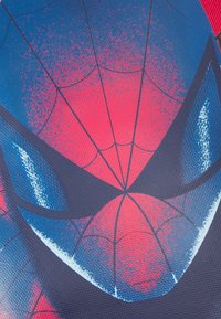 Zbliżenie maski Spider-Mana w kolorze czerwonym i niebieskim, z czarnymi wzorami pajęczyny oraz odbijającymi się refleksami na teksturowanej tkaninie.