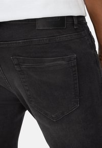 Schwarze Denim-Jeans mit einer Gesäßtasche, die leicht akzentuiert gesteppt ist, und einem gut sichtbaren Lederlabel am Bund.