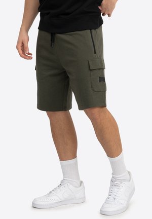 Olive green cargo shorts made of soft fabric, featuring side pockets, a zip pocket, and stitched details. Paired with white sneakers and socks.