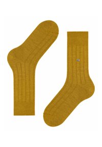 Calzini di cotone giallo senape con texture a coste e finitura liscia. Presentano un piccolo dettaglio del logo in argento su un calzino.