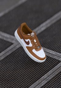 Rudono odinė tenisų bateliai su baltais akcentais, apvalia priekyje, perforacijomis, raištelių uždarymu ir Nike Air logotipu ant liežuvio ir šono. Tekstūruotas padas.