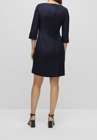 Robe bleu marine avec des manches trois-quarts et une coupe ajustée. Possède une fermeture éclair au dos et un motif texturé subtil.