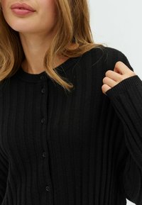 Black ribbed cardigan with a crew neckline, featuring button closures and long sleeves, made of a soft fabric with subtle texture.