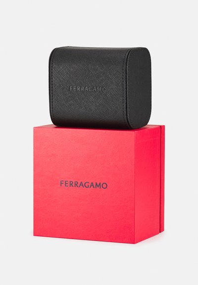 Black textured leather cosmetic case with embossed "Ferragamo" logo, placed on a red box featuring black "Ferragamo" branding.