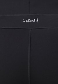 Fekete sportleggings széles derékrésszel, rajta "casall" logóval, sima textúrával és varrási részletekkel a fokozott tartósság érdekében.
