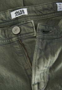 Maslinasto zelene traperice s patentnim zatvaračem, kopčanjem na dugme i oznakom "JACK & JONES." Imaju teksturirani materijal i izražene detalje šivanja.