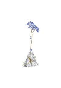 La base in cristallo trasparente con accenti dorati presenta un gambo sottile e curvo che sostiene tre fiori blu con centri gialli e una goccia di cristallo blu.