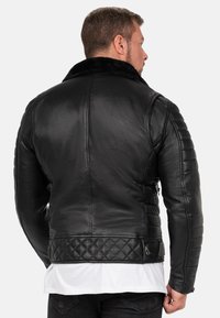 Zwarte leren jas met een geknoopt lagere rand, gestructureerde mouwen en een kraag van nepbont. Bevat een ritszak en heeft een gladde afwerking.