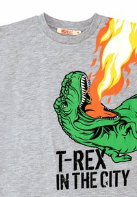 Camiseta de algodón gris con un gráfico de un T-rex verde rodeado de llamas naranjas y texto negro que dice "T-REX EN LA CIUDAD."