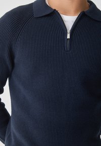 Námořnický ribkovaný pletený pulovr s límcem na zip a strukturovaným střihem, s texturovanou tkaninou a klasickým designem.