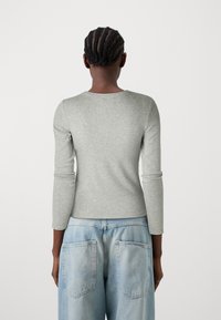 Haut à manches longues gris clair avec un col rond, présentant une texture lisse. Assorti à un jean large taille haute bleu clair.