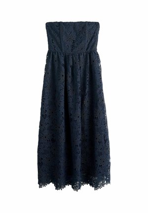 Tumši zila mežģīņu kleita ar bezsiksniņu dizainu un ziedu rakstiem, pieguļoša virsdaļa un plūstoša svārku daļa. Aprīkota ar viļņveida apakšmalu un faktūru audumu.