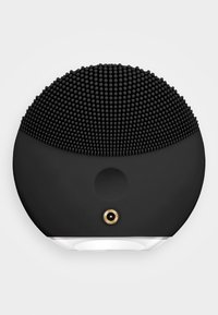 Svart silikon ansiktsrensende enhet med en teksturert, prikkete overflate og en glatt bunn. Har et gull tilkoblingspunkt og hvite accenter.