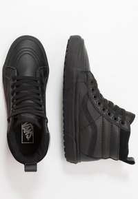 Černé vysoké tenisky Vans, jedny zhora a druhé z boku, na bílém pozadí.