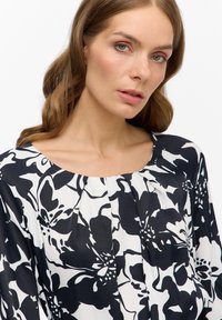 Schwarz-weiße Bluse mit Blumenmuster, runder Halsauschnitt, Falten auf der Vorderseite und glattem, leichtem Stoff.