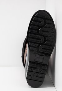 Semelle de chaussure noire avec un motif de crampons profonds, nom de la marque "GUESS" embossé, taille 37, et une partie de la tige de la botte à imprimé léopard visible.