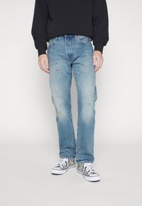 Jeans azul claro con corte recto, que presentan un ligero desvanecimiento y áreas desgastadas. Combinados con zapatillas de rayas negras y blancas.