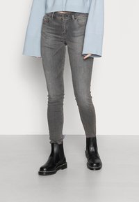 Jeans ajustados de mezclilla gris con una cintura de altura media, combinados con botas chelsea negras. El material es suave, con un ligero desgaste y sin adornos visibles.