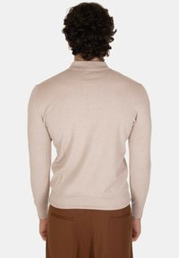 Maglione beige a maglia con un design aderente e maniche lunghe, caratterizzato da un colletto a coste. La texture appare liscia e leggera.