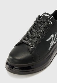 Chaussures synthétiques noires à bout rond, dotées d'accents métalliques, de lacets noirs texturés et d'une semelle épaisse et brillante.